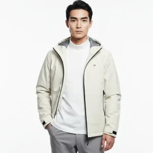 一名亞洲男性穿著米白色連帽機能夾克,左胸是KOMIA 品牌LOGO,內搭白色高領上衣與灰色長褲。